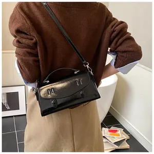Detailed view of black leather messenger bag worn on shoulder in a warm indoor setting