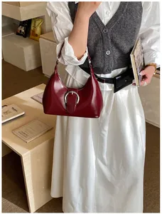 Détail du sac à main en cuir verni bordeaux avec boucle argentée ovale et poignée