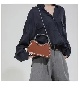 Brown leather crossbody bag with silver rivets and metal chain shown on a model