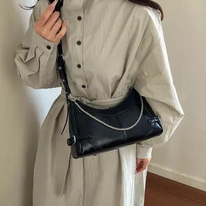 Sac demi-lune en cuir noir avec chaîne argentée porté par un mannequin à l'épaule