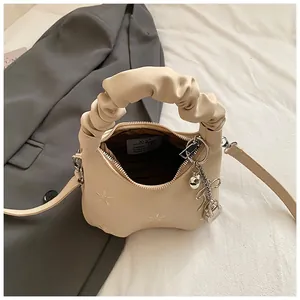 Close-up of beige handbag featuring delicate floral embroidery and a ruched handle detail