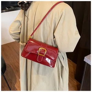 Détail d'un sac à bandoulière en cuir verni rouge avec une grande boucle dorée