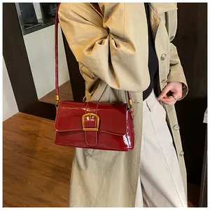 Détail du sac à bandoulière en cuir verni bordeaux avec grande boucle dorée et sangle