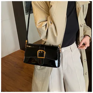 Détail d'un sac sous le bras en cuir verni noir avec boucle fer à cheval dorée