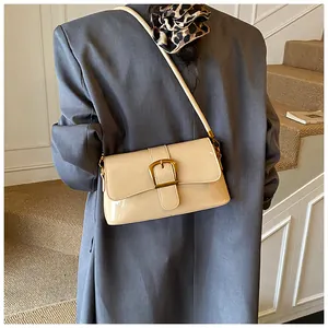 Détail d'un sac sous le bras en cuir verni crème avec boucle dorée porté sur un blazer gris