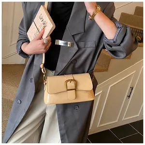 Sac à épaule chic en cuir verni crème avec boucle dorée porté sur un blazer gris