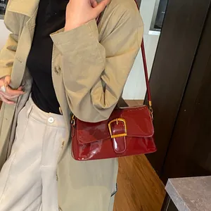 Sac sous le bras en cuir verni bordeaux brillant avec boucle dorée sur un manteau beige