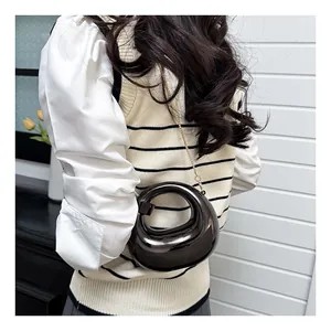 Detail showing the glossy dark crescent bag with a gold chain on a model’s shoulder