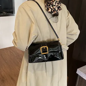 Sac sous le bras en cuir verni noir brillant avec boucle dorée porté avec un trench beige