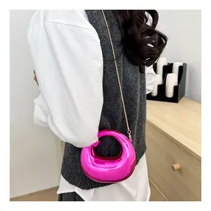 Detail of rose pink metallic crescent bag with gold chain strap on a wooden cabinet