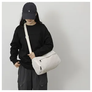 Mannequin portant un sac bandoulière cylindrique en nylon crème avec zips noirs