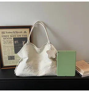 Détail d'un sac cabas blanc avec étoiles et broderies à côté d'une tablette