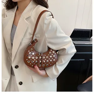 Detail of silver rivets on a brown crescent shoulder bag worn with a light blazer