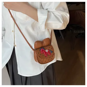 Détail d'un mini sac selle marron avec nœud en cuir et broderie poney sur chemise blanche
