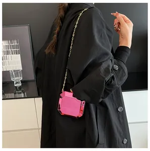 Detail of fuchsia geometric acrylic crossbody bag with gold chain on black coat