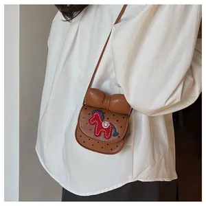 Détail du mini sac selle à pois avec nœud marron et cheval brodé porté par un mannequin