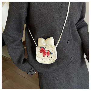 Détail du mini sac selle à pois noirs avec un grand nœud et broderie de cheval rouge
