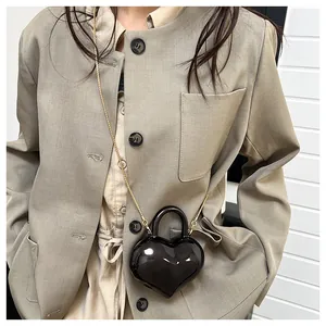 Detail of a shiny black heart-shaped mini bag with a gold chain and circular handle