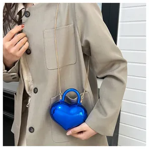 Blue heart-shaped mini crossbody bag with gold chain strap shown on a model