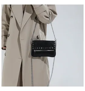 Detail of black rivet crossbody bag with silver chain strap on a trench coat