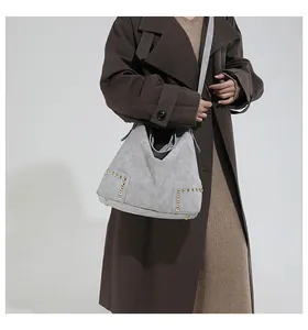 Detail of grey suede tote bag with golden rivets styled on a model wearing a brown coat