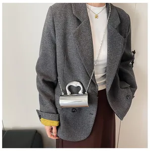 Detail shot of mini silver mirror cylinder bag with metal chain strap on model shoulder