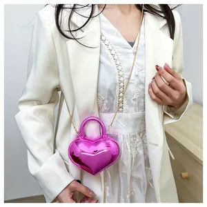 Detail of a bright pink heart-shaped mirror bag with gold chain strap on a model