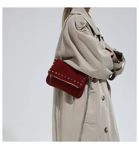 Detail of burgundy suede shoulder bag with silver studs and chain strap on a trench coat
