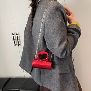 Mirror finish red cylinder handbag with heart handle and gold chain strap in hand