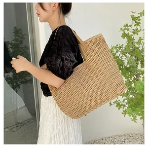 Detail view of large straw tote bag featuring beige weave texture and leather straps