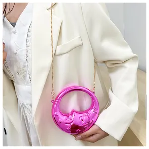 Detail of bright pink moon-shaped mini crossbody bag with gold chain on a model