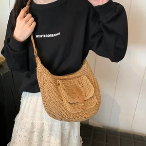 Handwoven straw shoulder bag in hobo style with leather flap pocket and thin brown strap