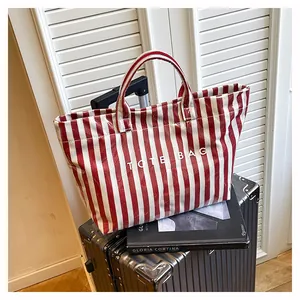 Détail d'un sac cabas à rayures rouges avec texture imperméable sur une valise argent