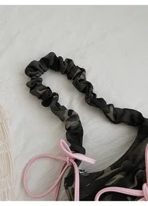 Close-up of camouflage baguette bag with ruffled shoulder strap and pink bow detail