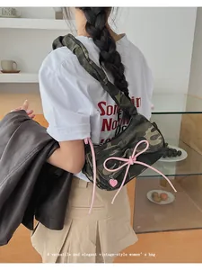 Detail of canvas camo shoulder bag featuring a pink bow and heart charm on a model