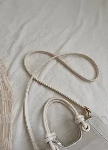 Detail of cream bucket bag showing knotted handle and textured PU leather finish