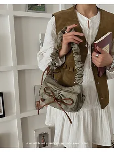 Detail of sage green ruched baguette bag with leather bow and cloud pleated shoulder strap
