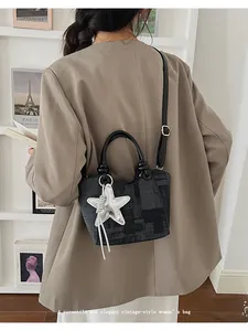 Detail of retro gray plaid bucket bag with silver star pendant on a white bookshelf