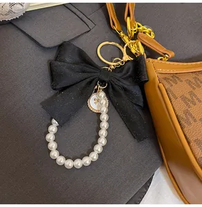 Detail of elegant black satin bow and pearl keychain accessory on a designer handbag