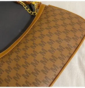 Close-up of brown textured leather underarm bag with M-logo print and gold chain links