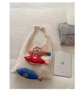 Close-up of cream knit tote bag featuring three colorful knitted fish charms on the side