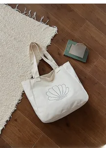 Detail of canvas tote bag with silver rivet shell design on a rustic wooden background