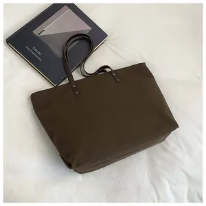 Detailed view of dark brown canvas tote bag with metal rivets on minimalist cotton background