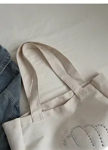 Detail of off-white canvas tote with reinforced shoulder straps and silver rivet accents