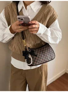 Brown monogram underarm bag with black bow and pearl charm on a stylish model