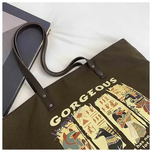 Close-up of canvas tote bag featuring Egyptian Anubis motifs and leather handles
