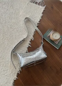Chic silver metallic patent leather shoulder bag on a white fringe rug in a cozy setting