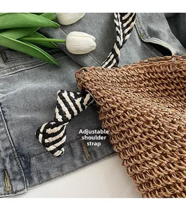 Detail view of woven straw tote bag featuring adjustable black and white striped cotton strap