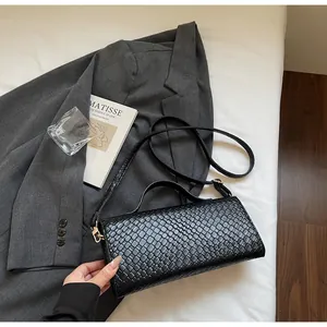 Dettaglio borsa nera con trama intrecciata e hardware dorato su sfondo di lenzuola bianche
