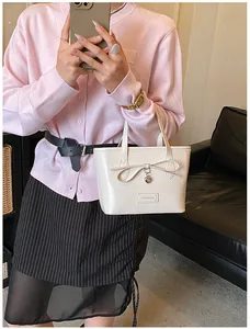 Close-up of cream tote bag featuring a bow detail, heart pendant, and Fashion label patch